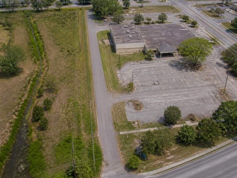 Aerial view of a redevelopment parcel in Pensacola, Florida, with an older commercial building, vacant parking, road access and drainage land.